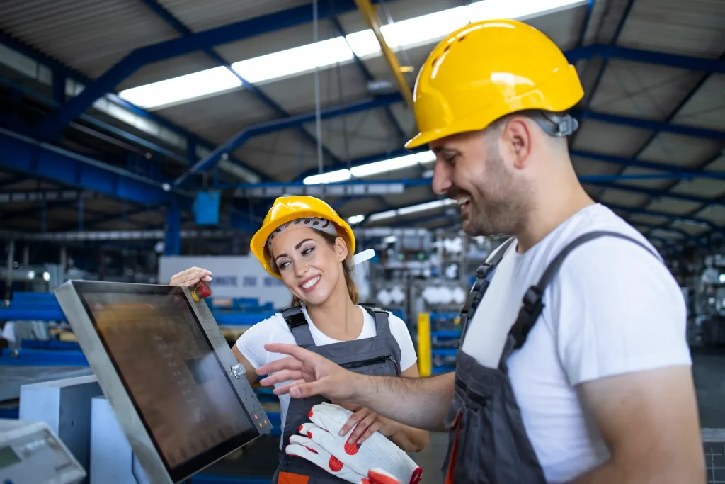 factory worker explaining trainee how to operate industrial machine using new software touch screen computer